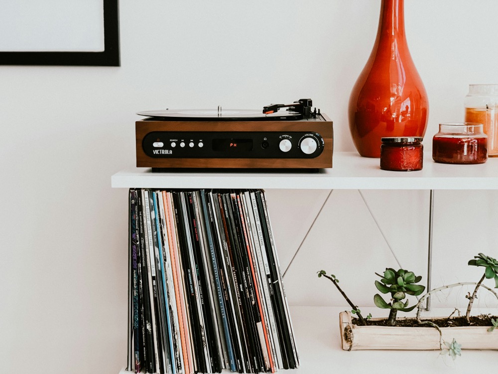 Plattenspieler auf einem weißen Regal, darunter Schallplatten, daneben eine orange Vase