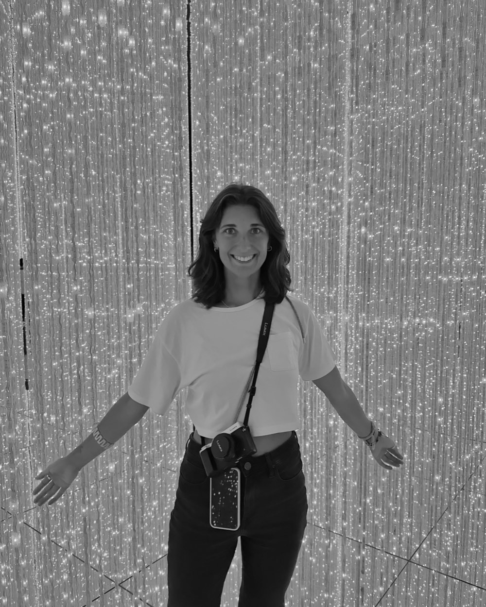 Angelina Hoppe lachend mit Kamera in einem Raum voller Lichterketten, schwarzweiß